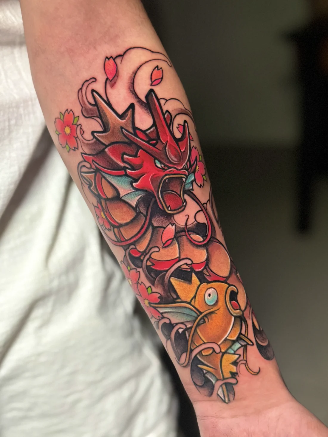 Tatuagem colorida do Gyarados e Magikarp de Pokémon com flores de cerejeira feita pela Jess Zanatta